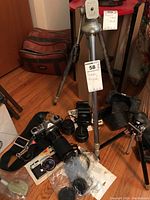 Photo of entire collection on wooden floor showing camera tripods, cases, lenses, camera body, flash, and accessories