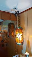 Full view of the double light hanging lamp installed on ceiling corner amid wood panel walls, one light glowing.