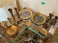 Overhead view showing assortment of miniature brass decorative plates, vases, candle holders, small trays, and other ornaments displayed on a metal rack.