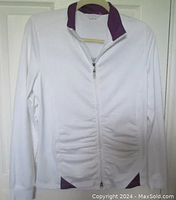 Full front view of white golf jacket with purple accents laid flat showing front zipper and ruching