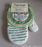 Oven glove showing Irish blessing text in green with Celtic knot border and 'Ireland' text at the top, folded with pot holder partially visible.