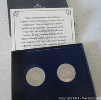Two silver-coloured commemorative coins in dark blue velvet inset inside black box. Informational card about Dofasco's 88-year history and company founding included.