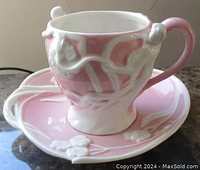 Angle view of the cup and saucer set showing the matching light pink tone and white raised floral details on saucer.