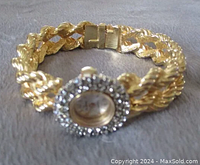 The full gold toned hinged clamper bracelet watch laid out to show the band contour and clasp mechanism.