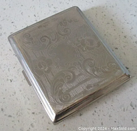 Closed view of the vintage silver cigarette case showing the paisley and floral etched design on the front.