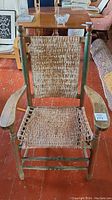 Full view of the antique wooden porch chair showing the woven seat and back, wooden armrests, and distressed green paint.