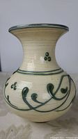 Side profile of artisan studio vase showing green vine and floral decoration on cream ceramic.