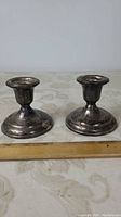 Front view of two short sterling silver candlesticks on a table, ruler indicates about 3 inches tall.