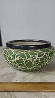 Side view of the ceramic flower pot showing green with abstract cream web-like pattern and dark rim.