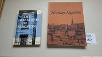 Two hardcover books placed side by side on a flat surface, one titled 'The Old Stones of Kingston' and the other titled 'Heritage Kingston' with an illustrated sepia-tone cover.