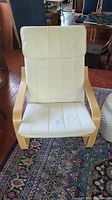 Front view of Ikea POÄNG chair showing beige fabric cushion and light wooden frame.
