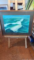 Full view of framed pastel painting of ocean waves on easel