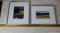 Both framed paintings side by side on table with ruler showing frame width of 10 to 13 inches