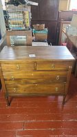 Front view of vintage wooden dresser showing four drawers with brass ring handles, medium brown finish, slight surface wear.