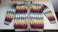 Front view of the multi color geometric hand knitted cardigan sweater laid flat showing full length and button detail.