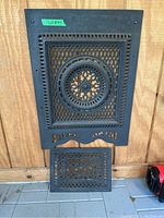 Both cast iron grates shown mounted on wood panel, large one above and smaller one below, displaying detailed lattice and floral designs with decorative edges.