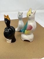 Front side view of the three ceramic pie birds, showing black bird with orange beak, plain white bird, and multicolor bird with yellow, blue, and pink accents.