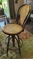 Side angle view of antique bentwood swivel chair showing cane seat and backrest, wooden framing, footrest and swivel base
