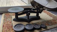 Side view of the antique cast iron balance scale with four weights displayed in front, showing the scale's structural details and weights distinctly labeled.