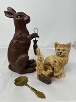 Photo of all items in the lot showing the large chocolate bunny mold with carrot, cat mold, small bunny figurine on stroller, and brass spoon