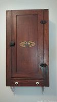 Full view of antique farmhouse wood cabinet, showing dark mahogany stain, rectangular door, and bottom drawer with white knobs