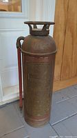 Full view of antique Essanay copper and brass fire extinguisher with side hose and handle on top.