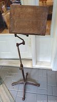 Front view of the antique lectern showing its wood top, adjustable rod, and cast iron four-legged base on tiled floor.