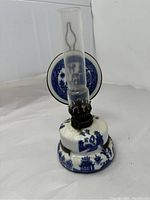 Front view of vintage Blue Willow ceramic oil lamp with glass chimney and circular reflector showing blue willow scene