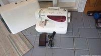 Full view of Brother XL-6452 sewing machine with hard white cover and black foot pedal on grey tiled floor.
