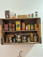 Overview of the wooden Coca Cola crate filled with various vintage grocery salesman sample tins and boxes.