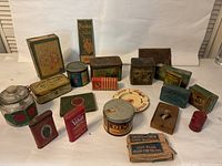 Overview of various vintage tobacco tins, cigarette boxes, snuff tins, and smoking accessories arranged on white background.