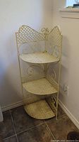 Front view of the cream-colored metal corner plant stand with 3 shelves.