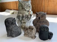 Front angle showing all five owl figurines on white surface with wood panel background.