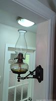 Side view of the vintage oil lamp mounted on a black metal bracket, showing clear glass chimney and round oil reservoir.