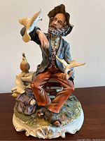 Full view of the figurine showing the man seated on the bench, feeding pigeons with detailed clothing and surrounding items.