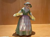 Clear front view of the figurine showing full dress and baskets of flowers.