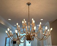 Frontal view showing full chandelier suspended by brass chain with 24 lit candle-style bulbs