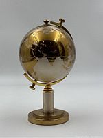 Front view of brass globe cigarette holder closed, showing engraved continents and polished brass finish.