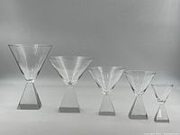 Single photo showing five Ekenas pyramid glasses of varying sizes from largest to smallest, clearly showing the distinctive pyramid-shaped stems and clear crystal bowls.