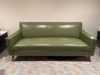 Full front view of green vinyl sofa against wall on tiled floor