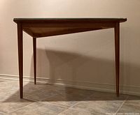 Side view of triangular teak table showing tapered legs and overall shape.