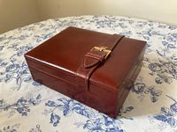 Closed box, three-quarter view showing burgundy leather exterior and gold-tone Rolex crown buckle