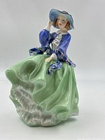 Front angle showing the figurine's facial features, hat, blue jacket, green skirt, and white underskirt.