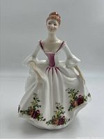 Front-facing view of the Royal Doulton Country Rose bone china figurine showing the floral decorated dress and seated pose with pink accents.