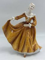 Front view of the Royal Doulton figurine showing young woman in amber dress holding dress edges.