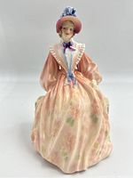 Front view of seated female figure wearing pink floral dress and wide-brimmed hat