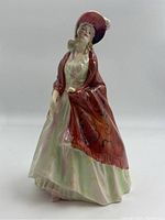Front and angled views of Royal Doulton The Paisley Shawl figurine worn red paisley shawl, pale dress and red hat with feather, glossy finish.