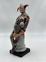 Side view of Royal Doulton 'The Jester' figurine showing detailed craftsmanship and seated position on gray column and black base.