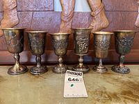 Six silver goblets displayed in a row with auction lot tag