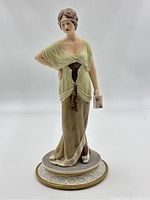 Front view of the vintage Capodimonte porcelain figurine showing woman in a green and brown dress holding a book.